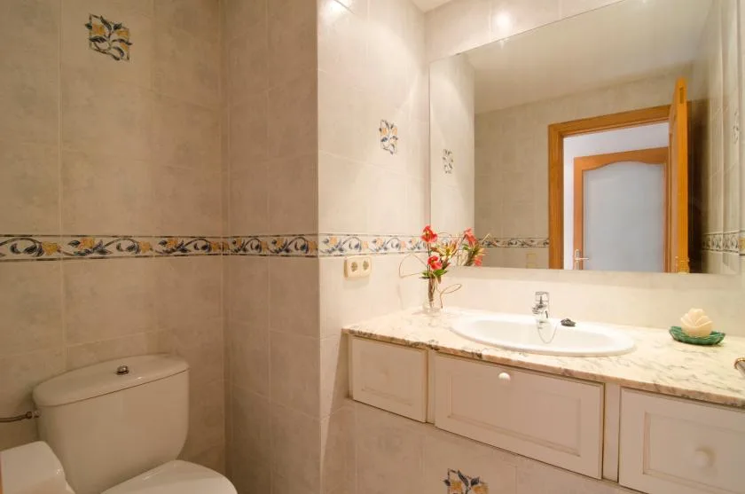 A tiled bathroom with a toilet, sink, and large wall mirror.