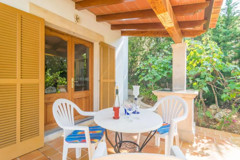 A covered patio with a round table, white seating, and garden greenery.
