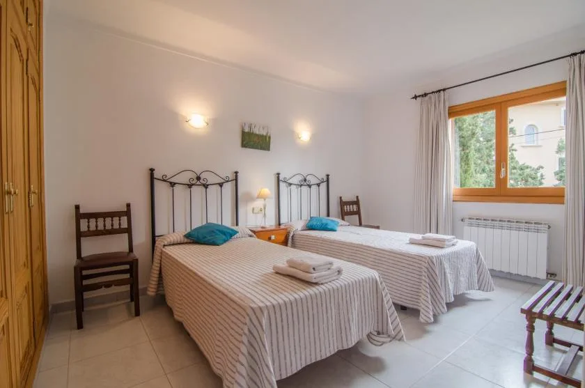 A bedroom with two single beds and a window overlooking greenery.