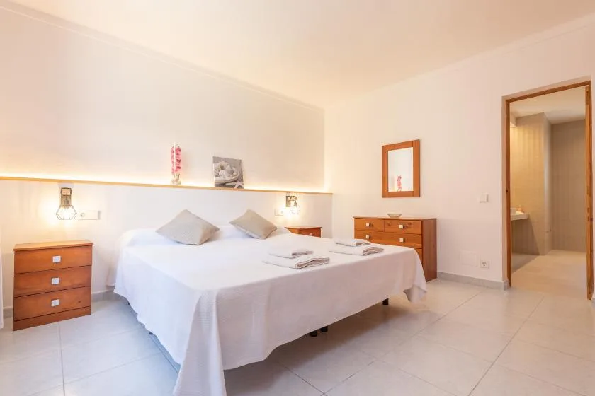 A bright bedroom with a large bed and wooden bedside furniture.