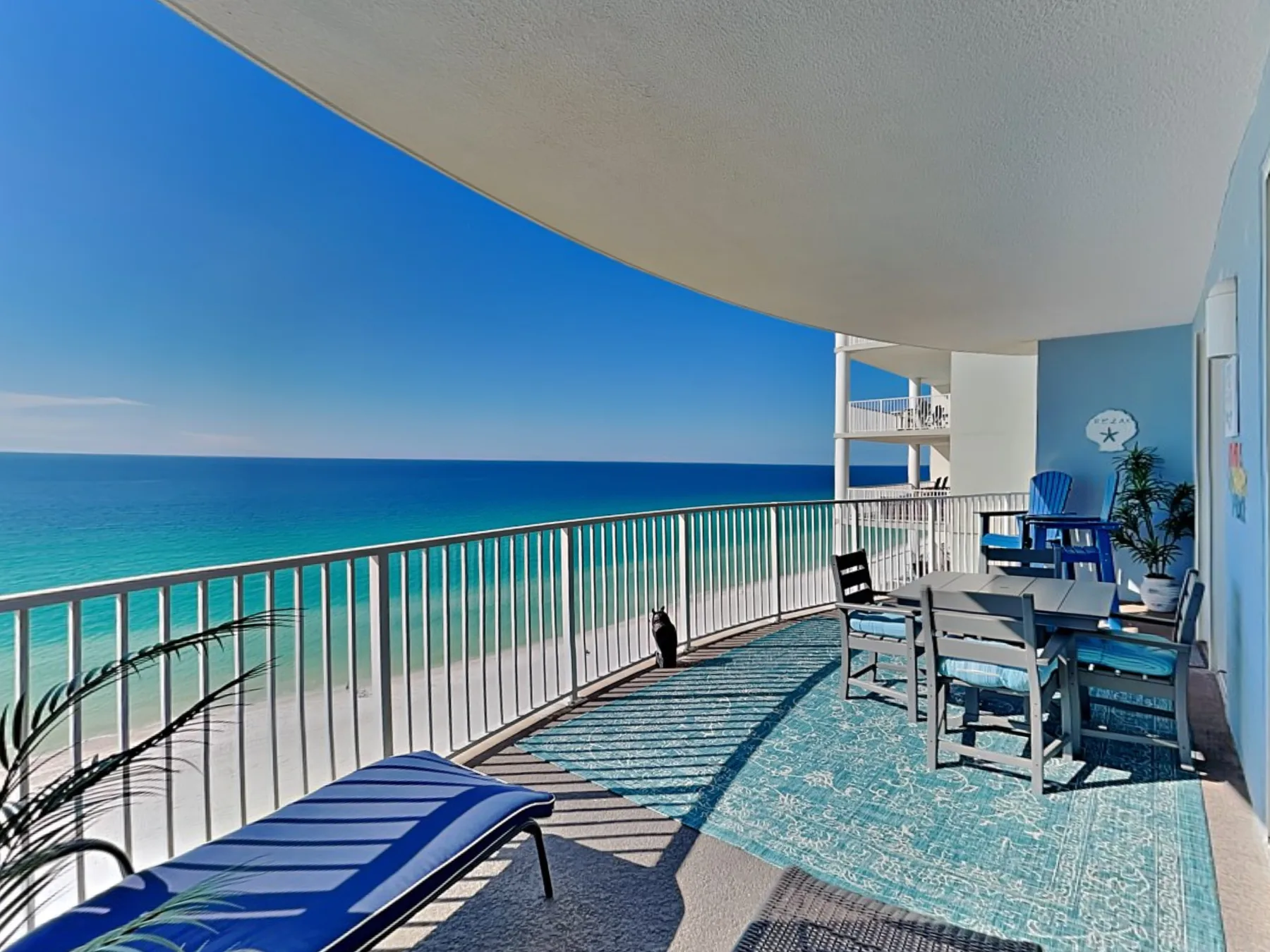 A sea-facing balcony has outdoor seating and a blue lounge chair.