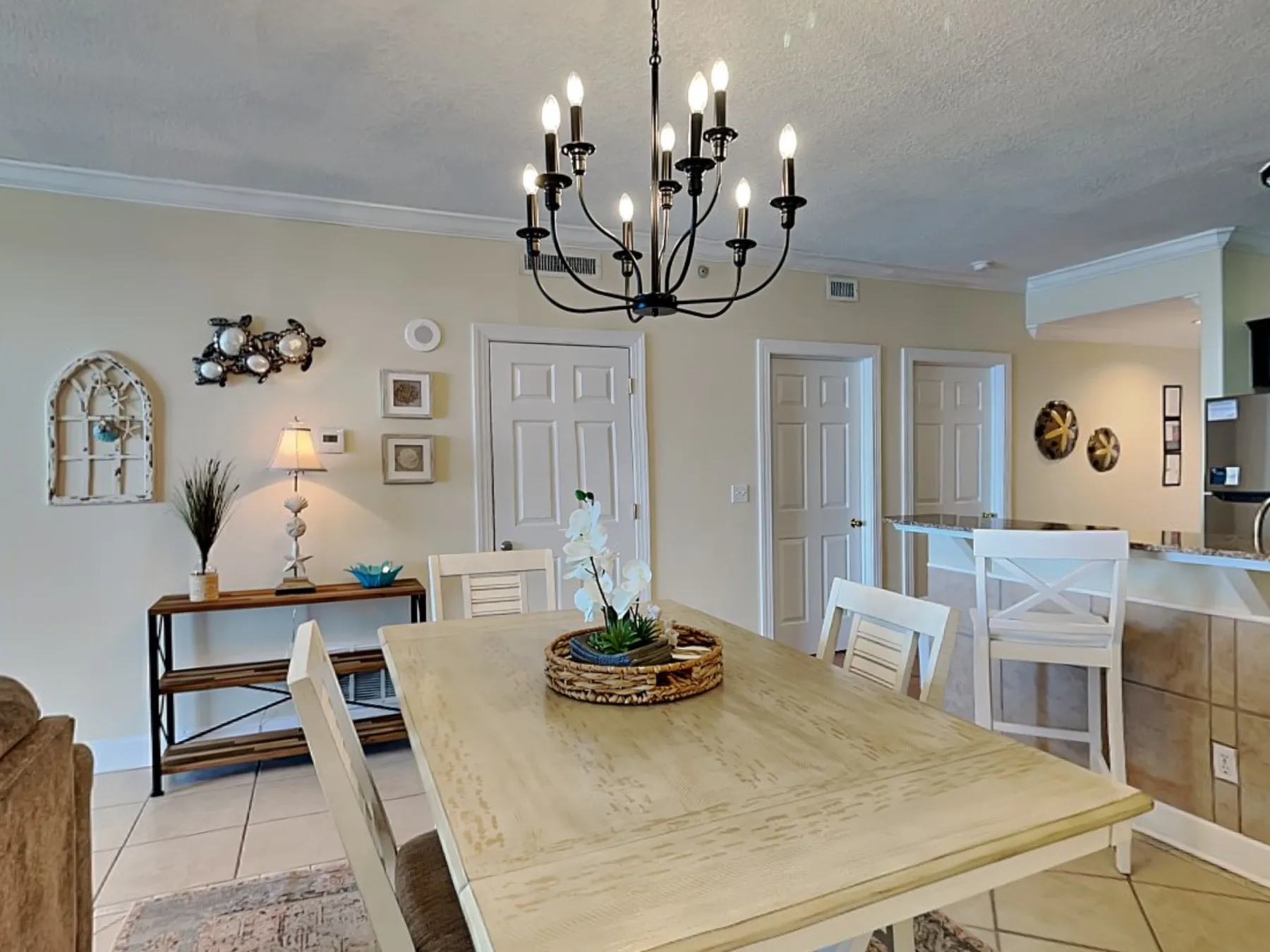 A bright dining area has a large table, surrounding chairs, and a hanging chandelier.