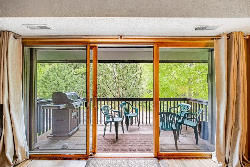 Sliding glass doors open onto a balcony with seating and greenery beyond.