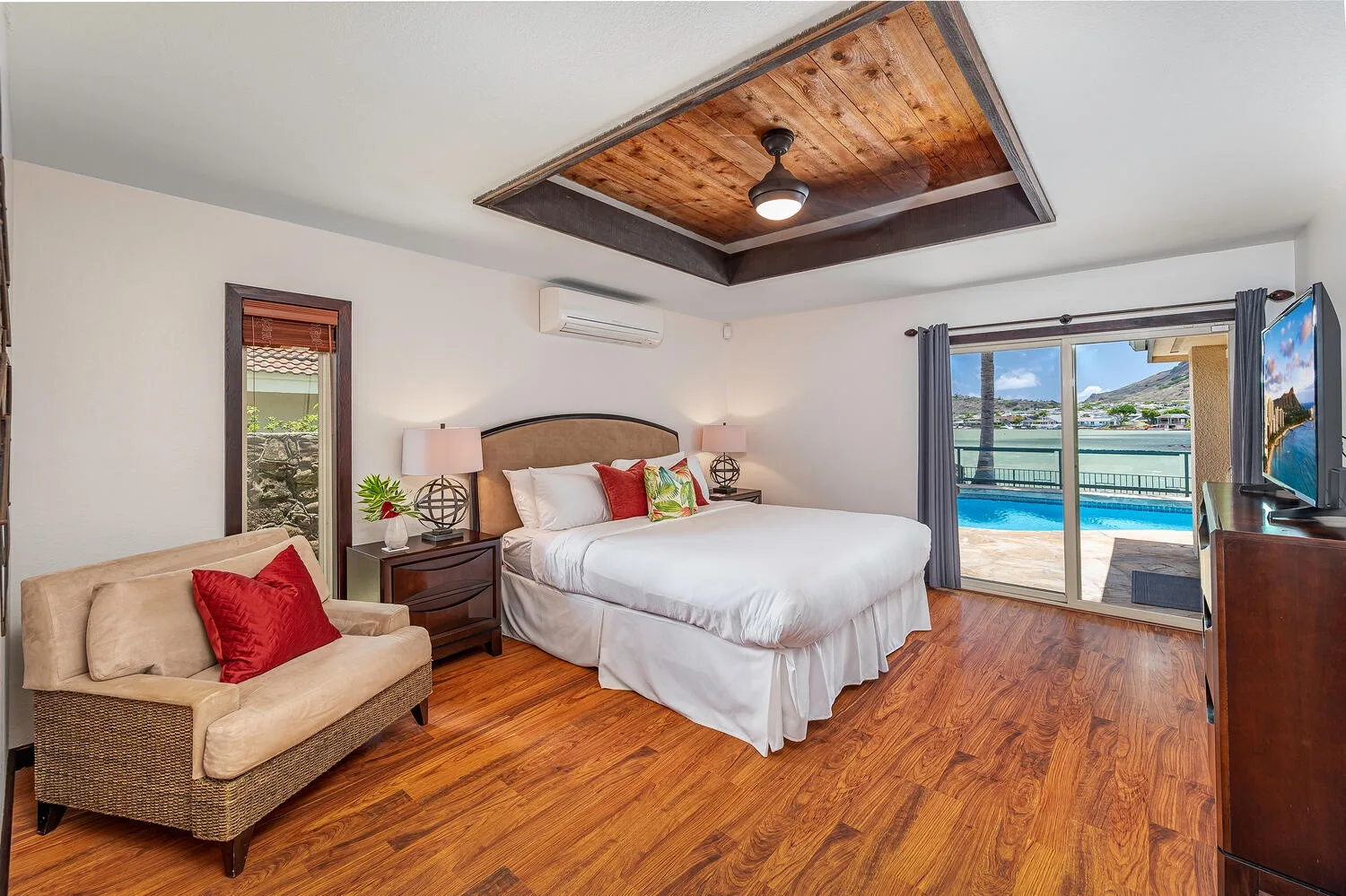 Un dormitorio con una cama, una zona de asientos acolchados y puertas de vidrio hacia una piscina.