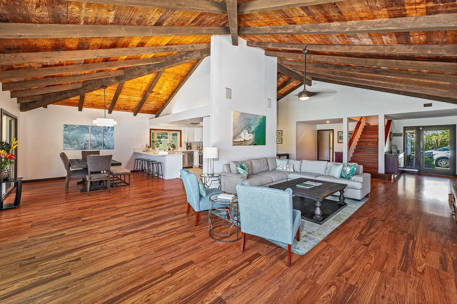 Sala de estar y cocina de concepto abierto, con asientos bajo vigas de madera expuestas.
