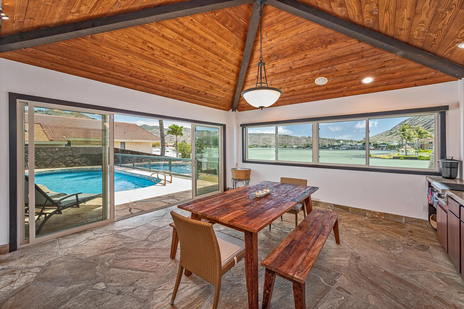 Un comedor con una mesa de madera da a una piscina a través de amplias ventanas.