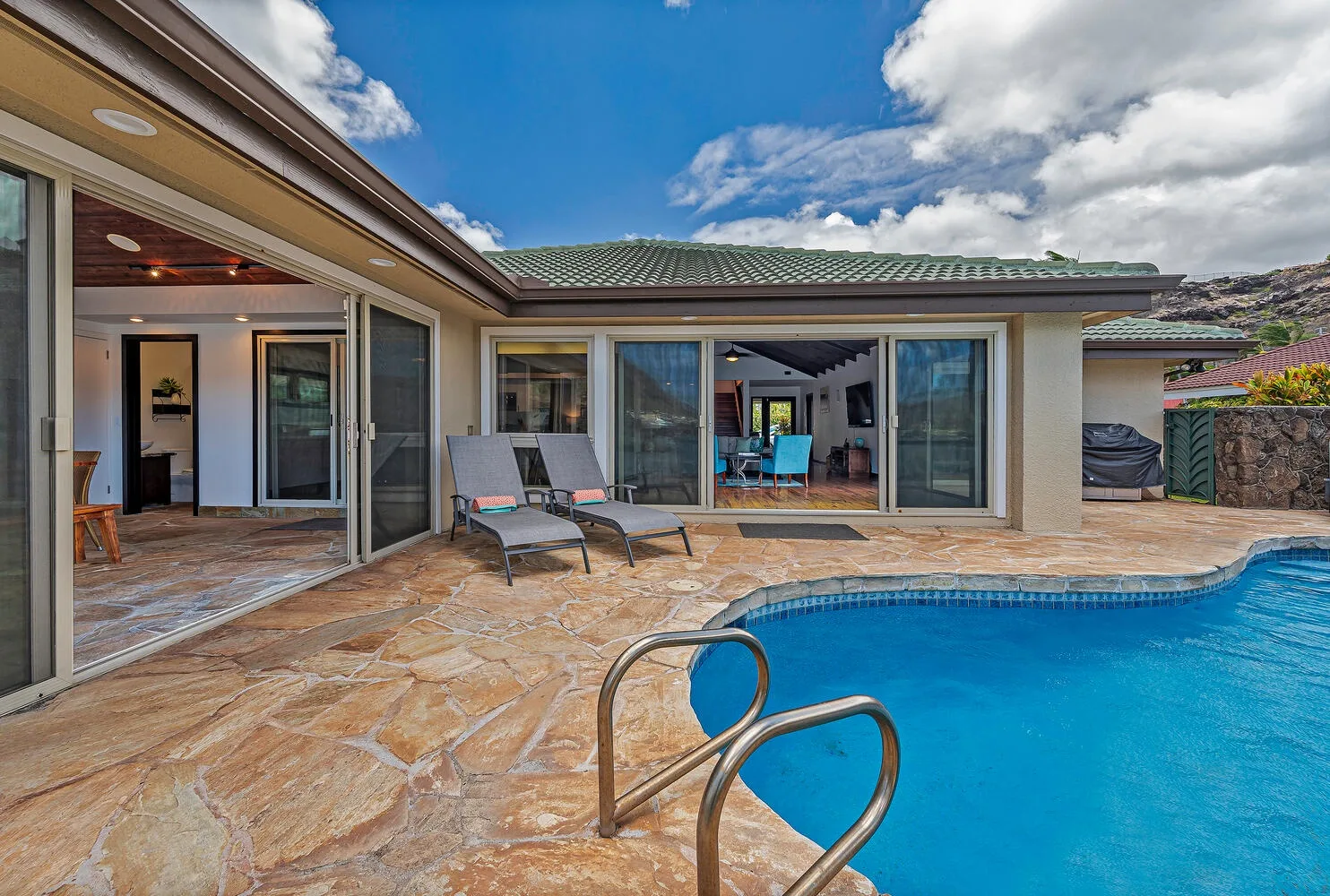 Una piscina junto a un patio pavimentado y una casa con puertas corredizas de vidrio.