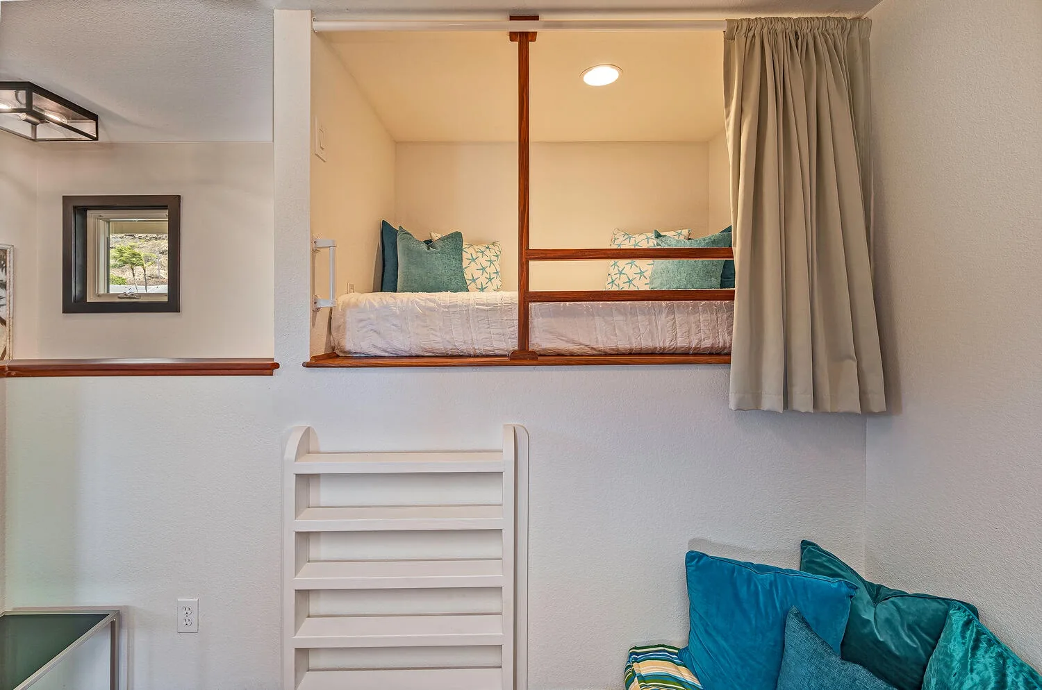 Un pequeño rincón para dormir con una cama elevada, cortina y asientos debajo.