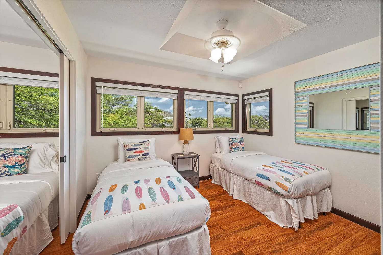 Un dormitorio luminoso con dos camas, ventanas grandes y ropa de cama colorida.