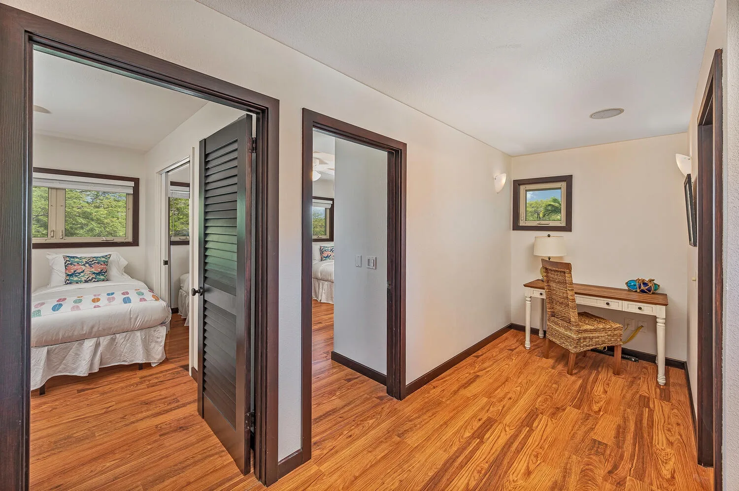 Una habitación luminosa con suelo de madera, escritorio y un dormitorio contiguo.