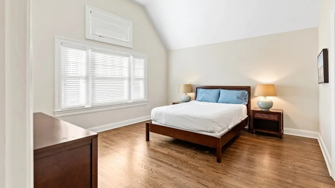 Un dormitorio con una cama, mesas de noche y ventanas con persianas.