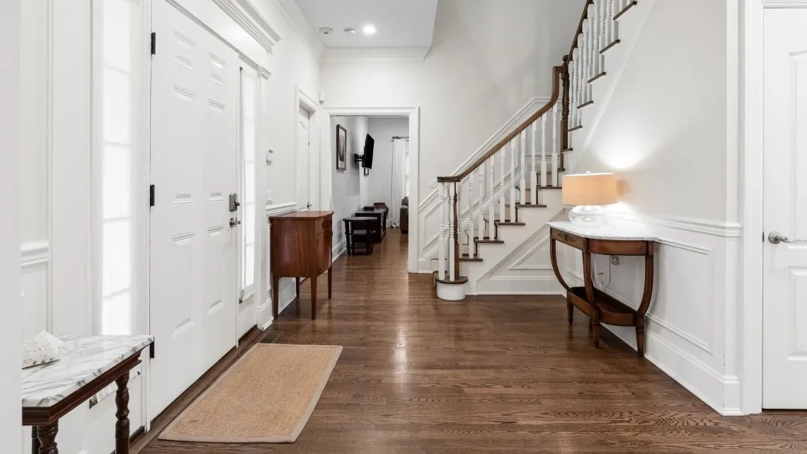 Un pasillo luminoso con suelo de madera y una escalera junto a la pared.