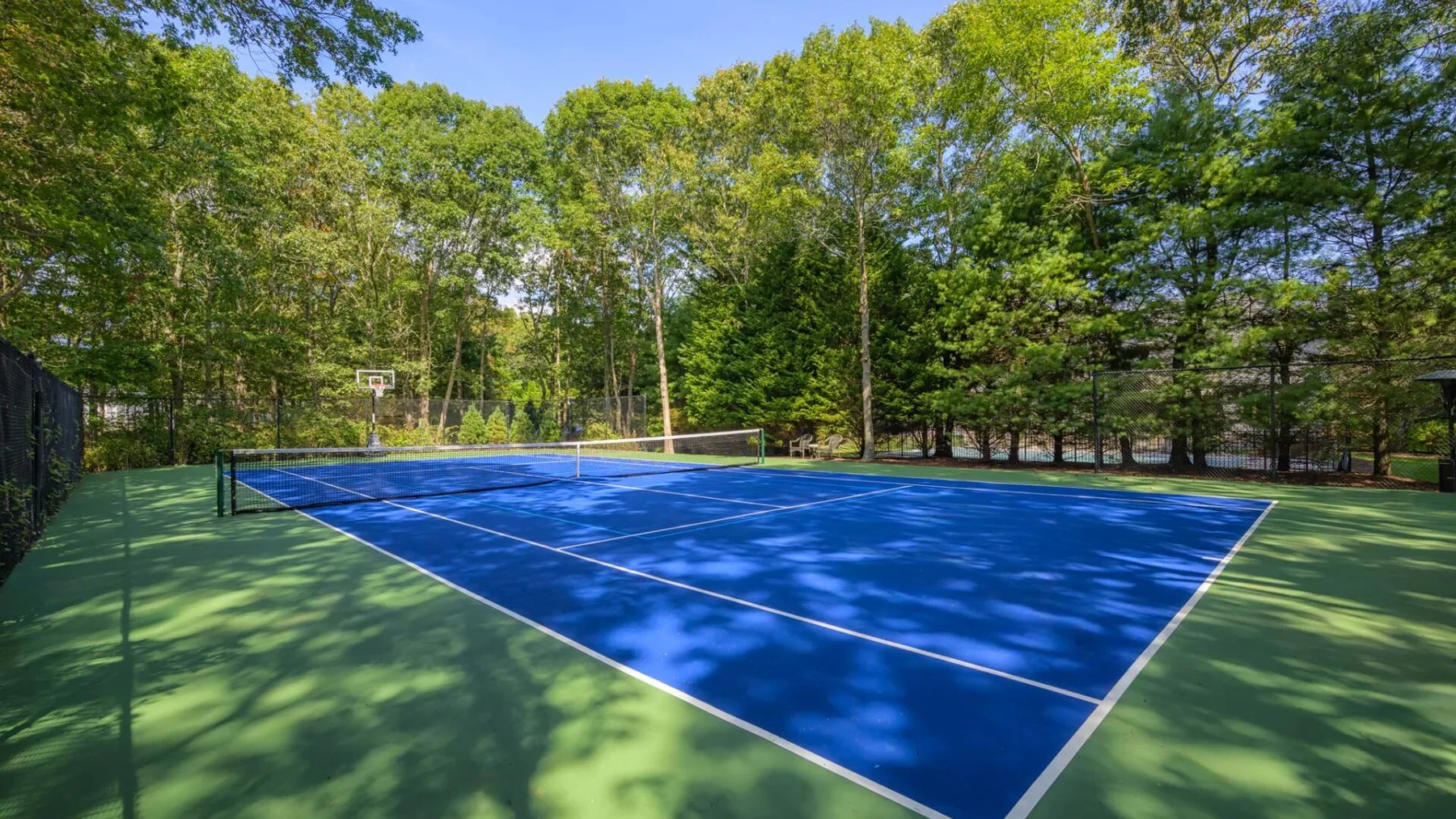 Una cancha de tenis azul al aire libre está rodeada de árboles verdes.