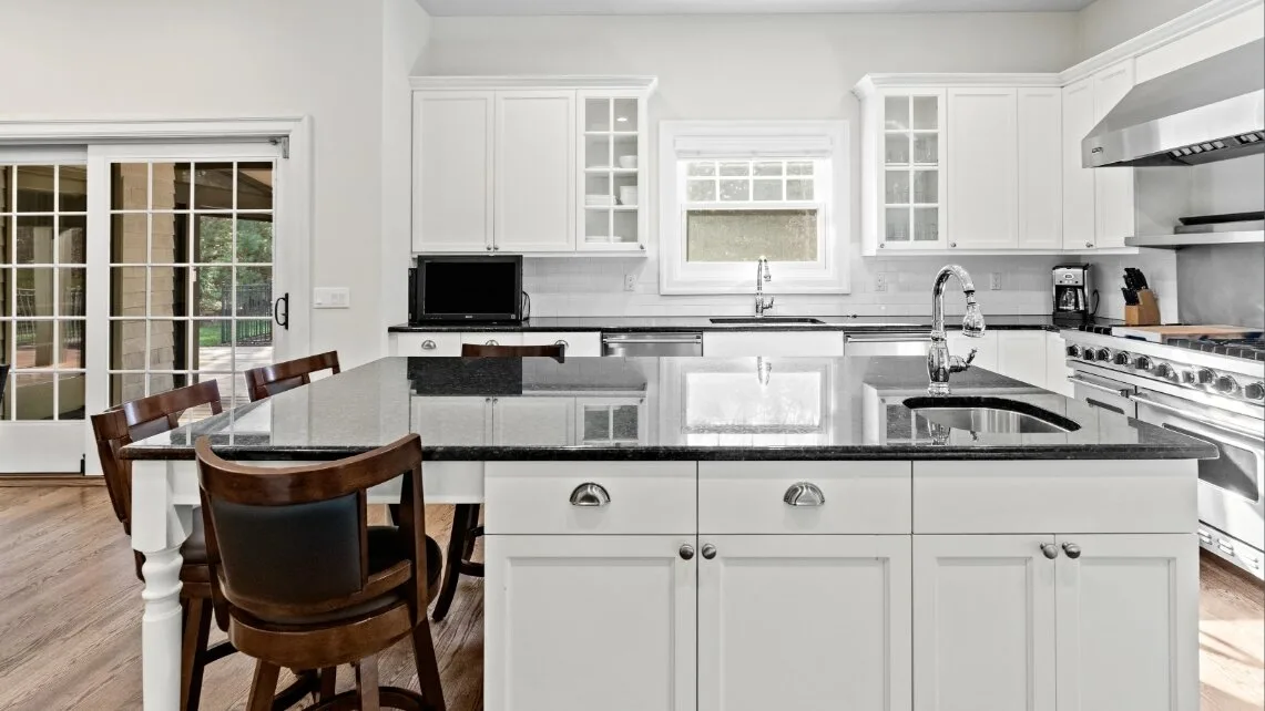 Una cocina luminosa con gabinetes blancos, una isla central y una mesa de comedor.