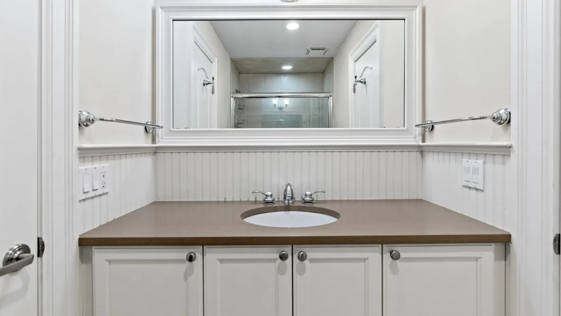 Un tocador de baño con un espejo amplio y un lavabo sobre la encimera.