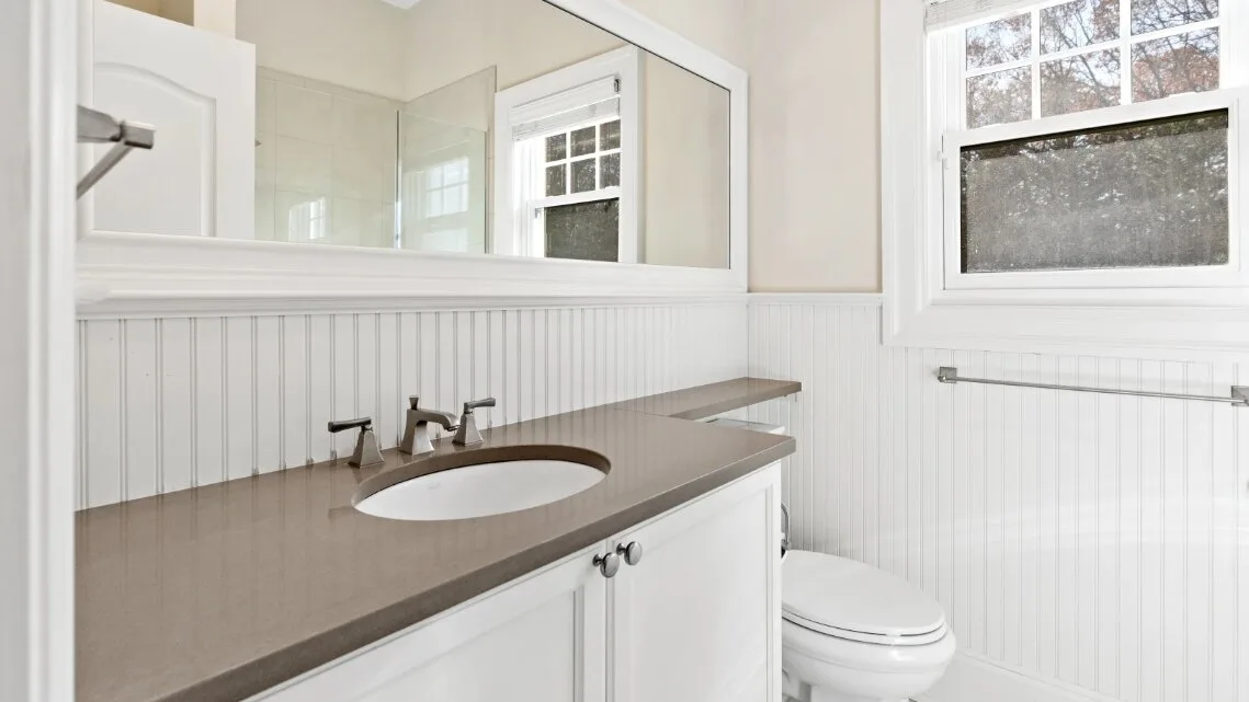 Un baño con una encimera larga, lavabo e inodoro junto a una ventana.