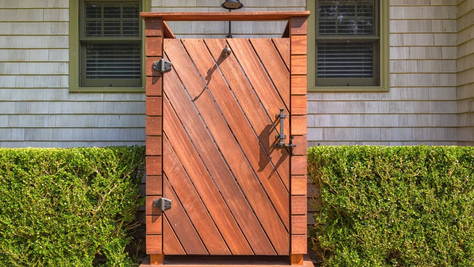 Una puerta de madera se alza entre setos podados junto a una casa.
