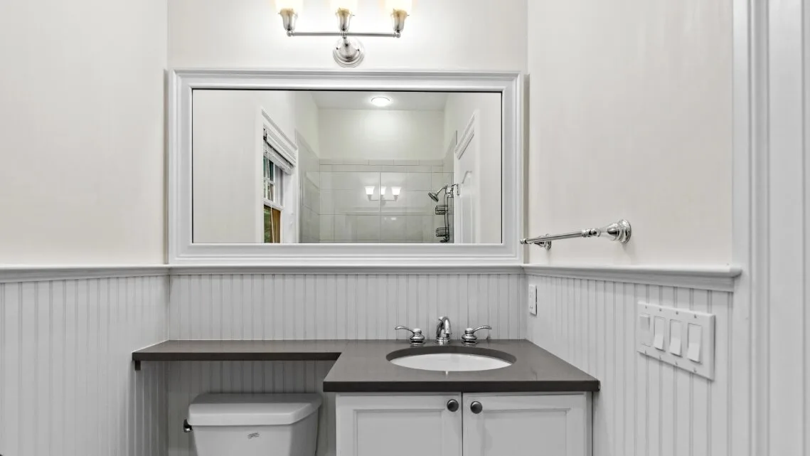 Un lavabo de baño luminoso con espejo, lavamanos y paredes con paneles.