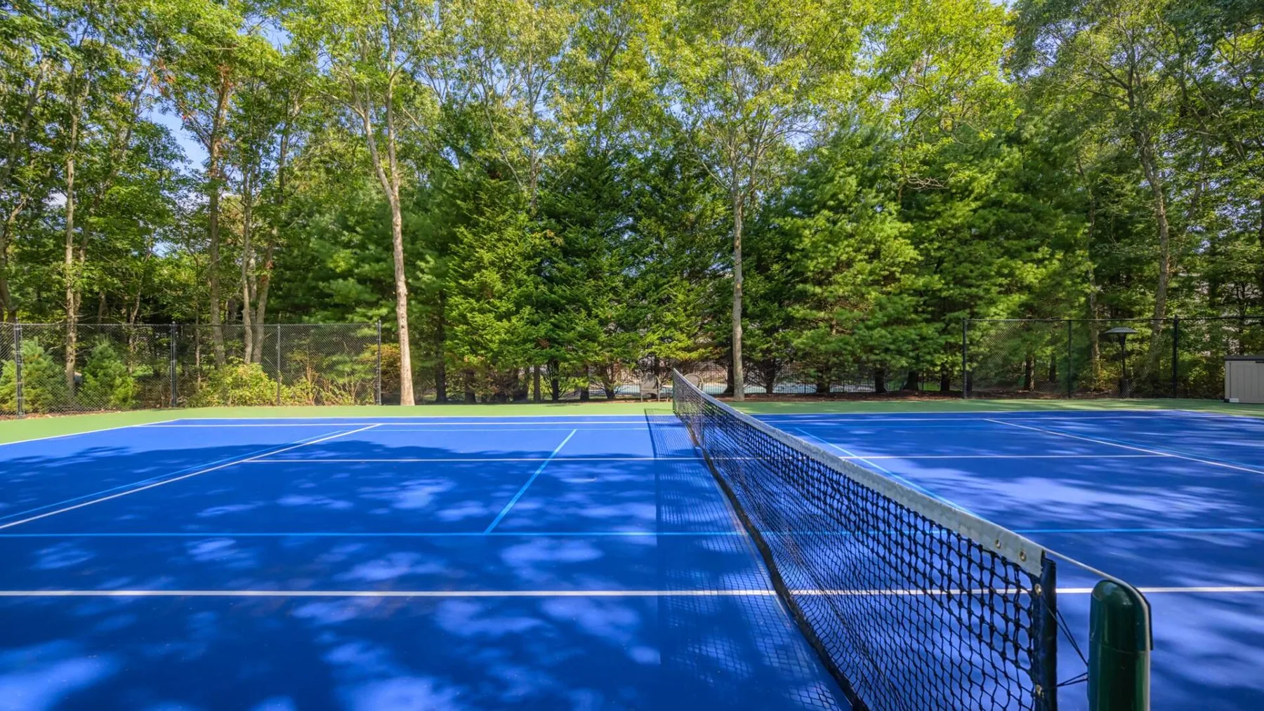 Una cancha de tenis al aire libre con una red, rodeada de árboles frondosos.