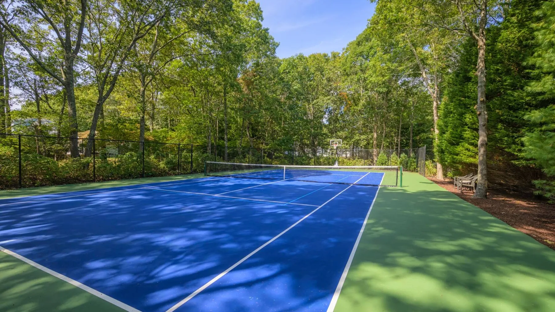 Una cancha de tenis al aire libre con superficie azul, rodeada de árboles.