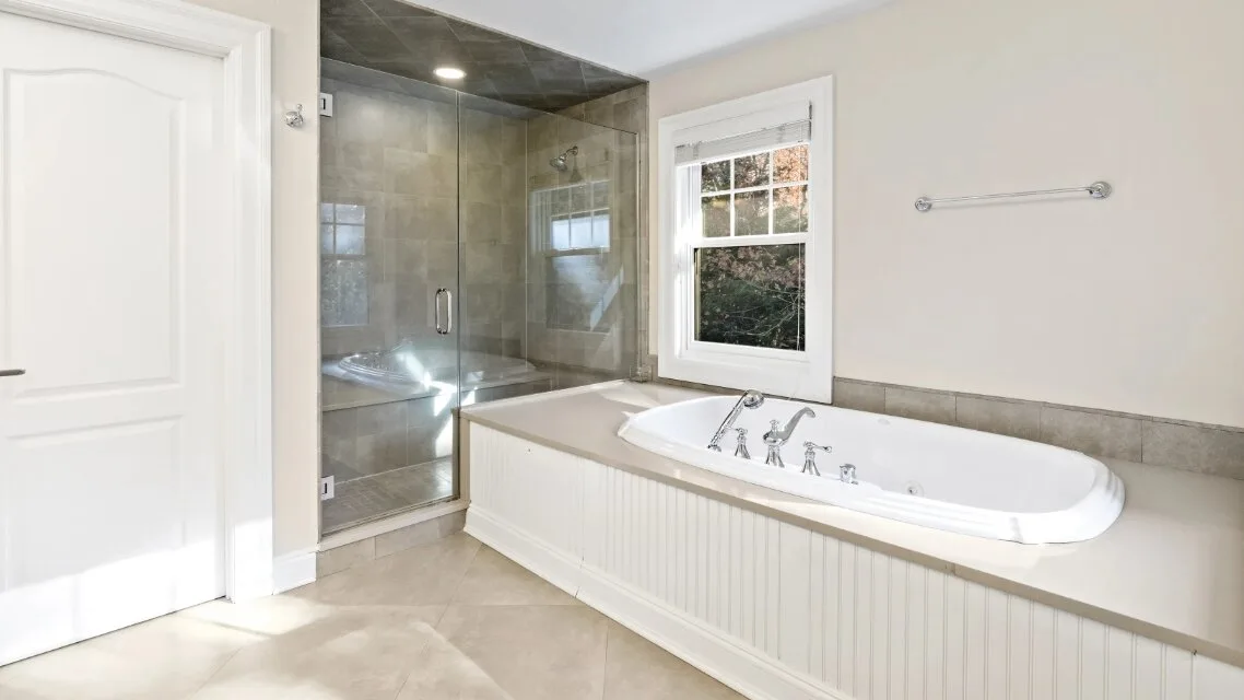 Un baño con bañera junto a una ducha de vidrio y una ventana.