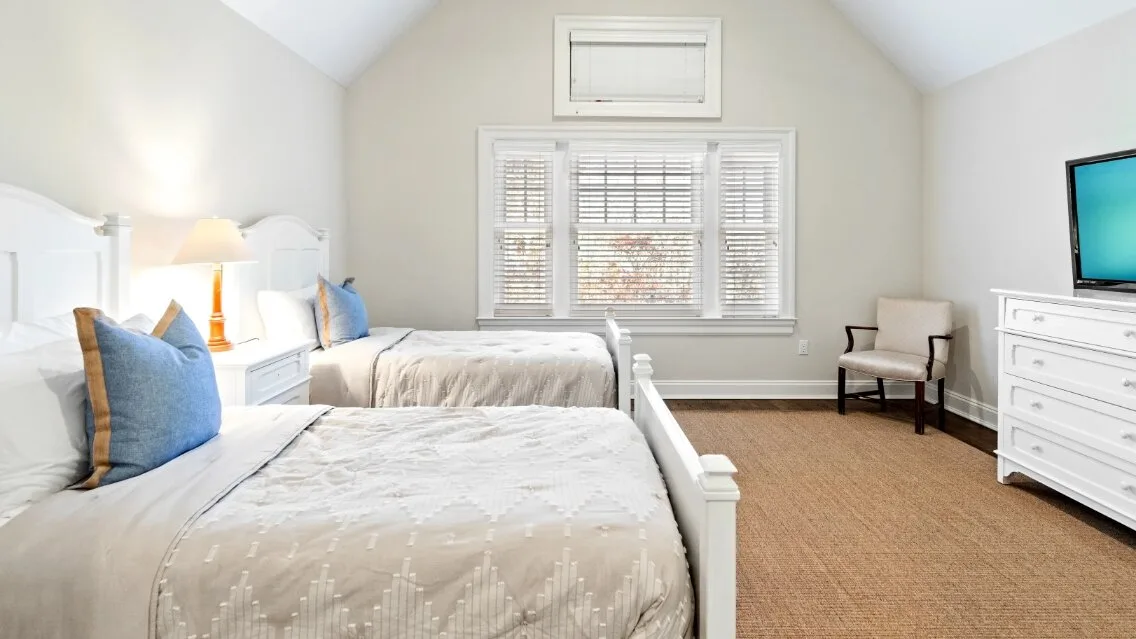 Un dormitorio luminoso con dos camas, una ventana y un televisor.