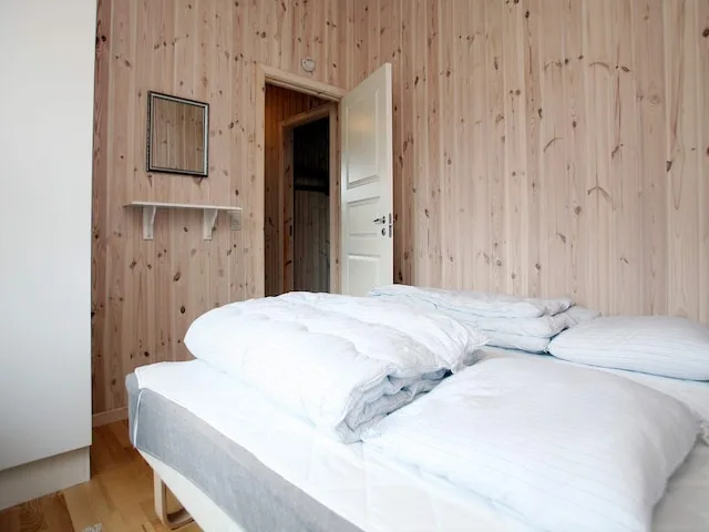 A bedroom with white bedding, wood-paneled walls, and an open door.