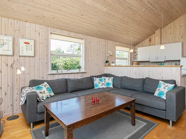 A living room with a sectional seating area and an open kitchen behind it.