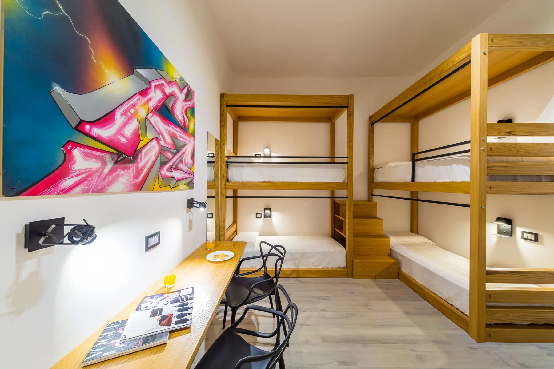 Un dormitorio con literas de madera y un escritorio bajo arte colorido en la pared.