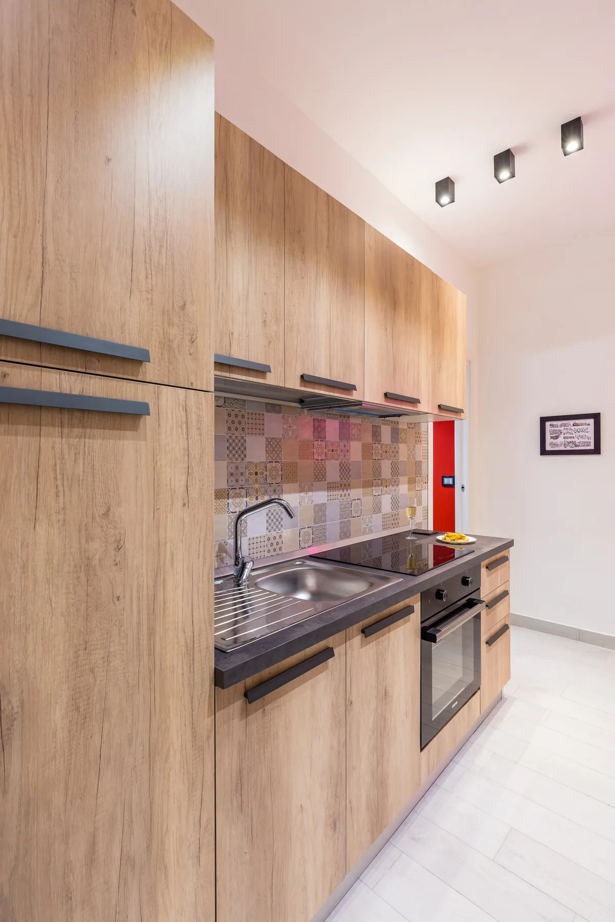 Una cocina compacta con gabinetes de madera, un salpicadero de azulejos y un fregadero de acero inoxidable.