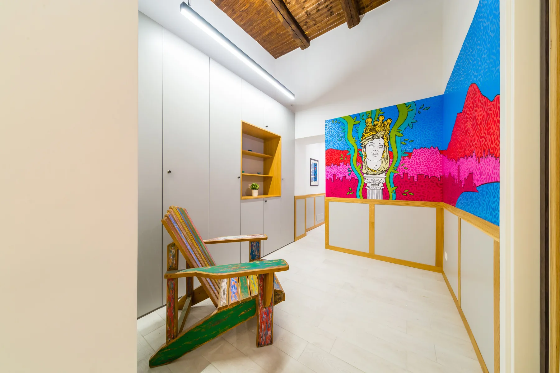 Una habitación luminosa con una silla de madera y un mural colorido en las paredes.