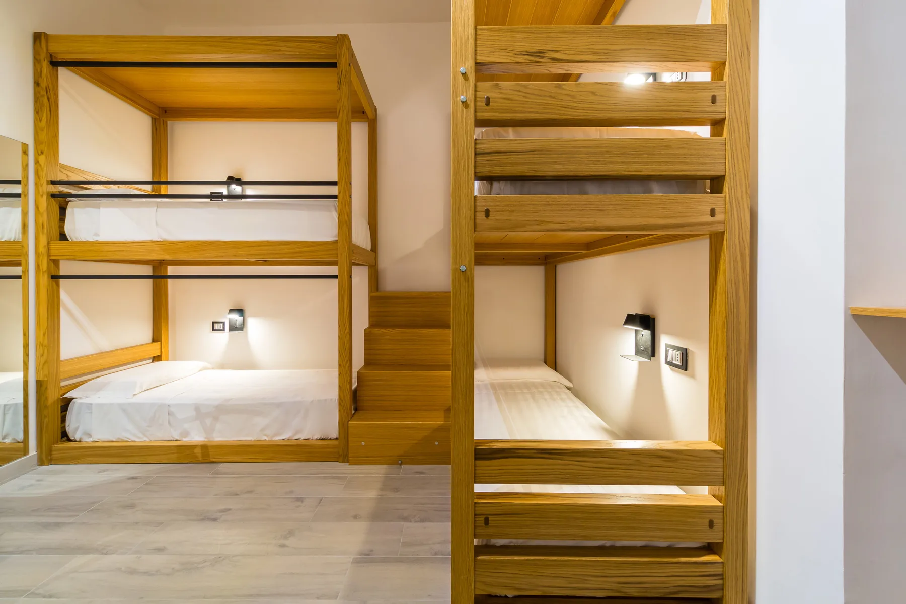 Una litera de madera con escalones incorporados está en un dormitorio luminoso.