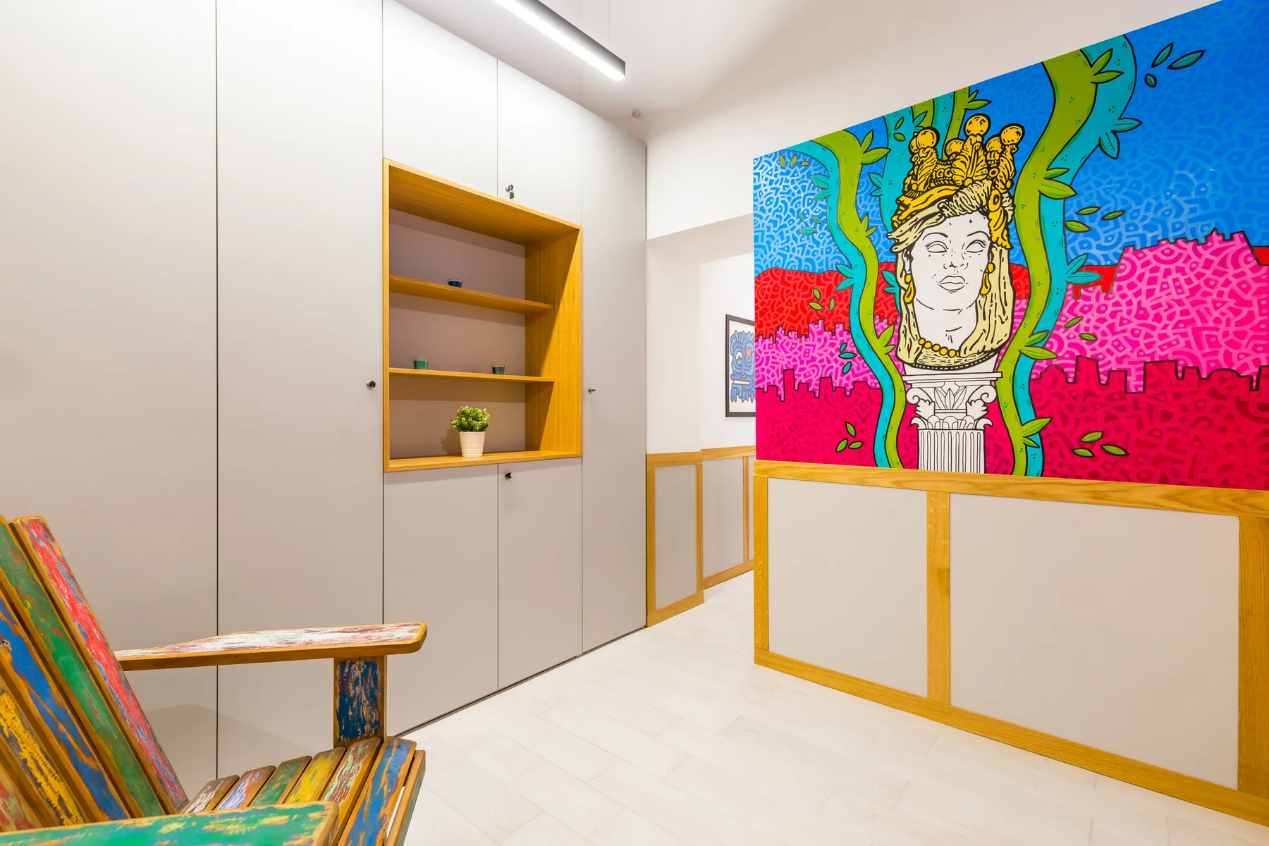 Un interior moderno y luminoso presenta un mural colorido sobre un separador y estantes empotrados.