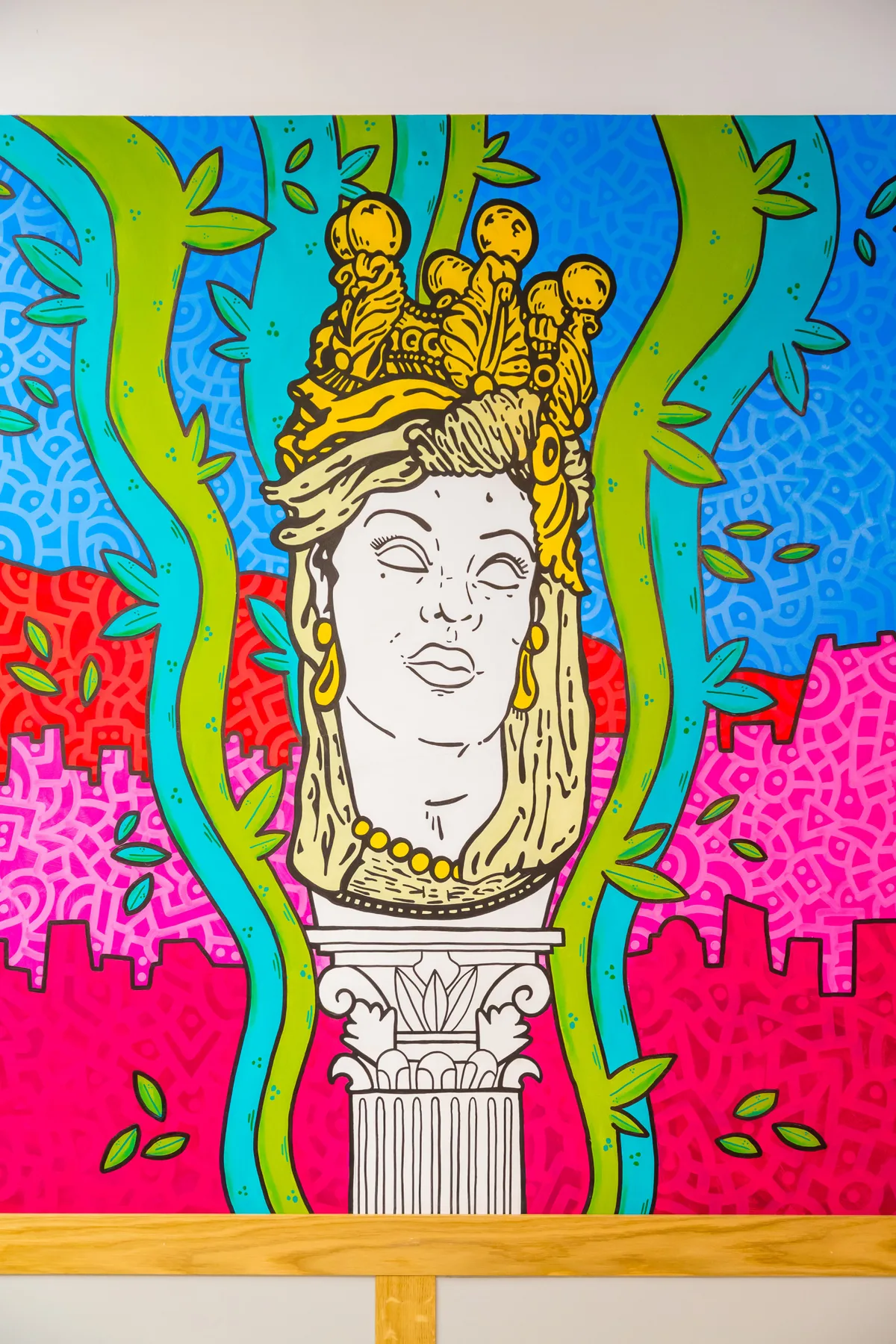 Un mural colorido muestra un busto clásico enmarcado por enredaderas verdes sobre un fondo estampado.