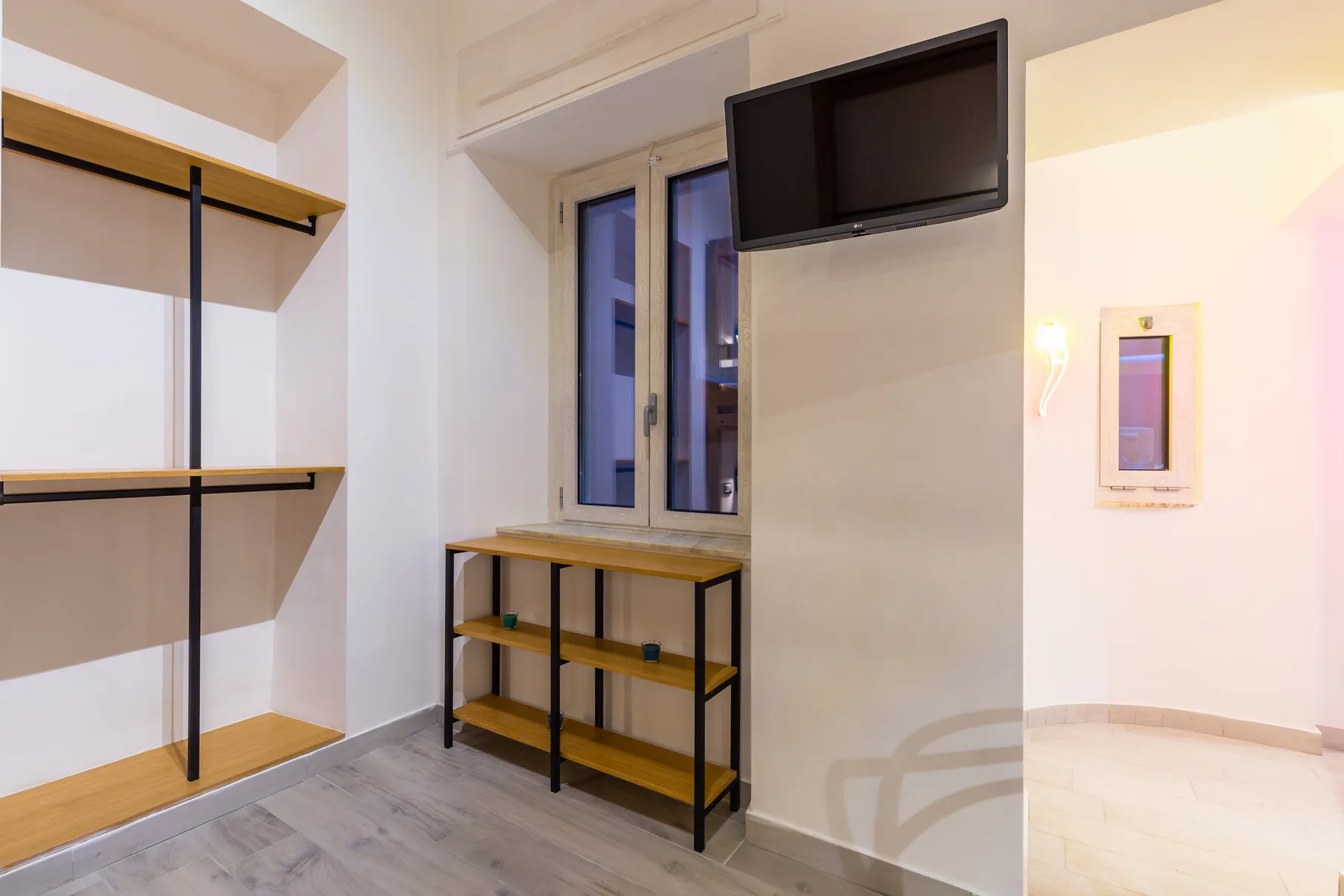 Una habitación luminosa con estantes abiertos, una mesa pequeña y un televisor en la pared.