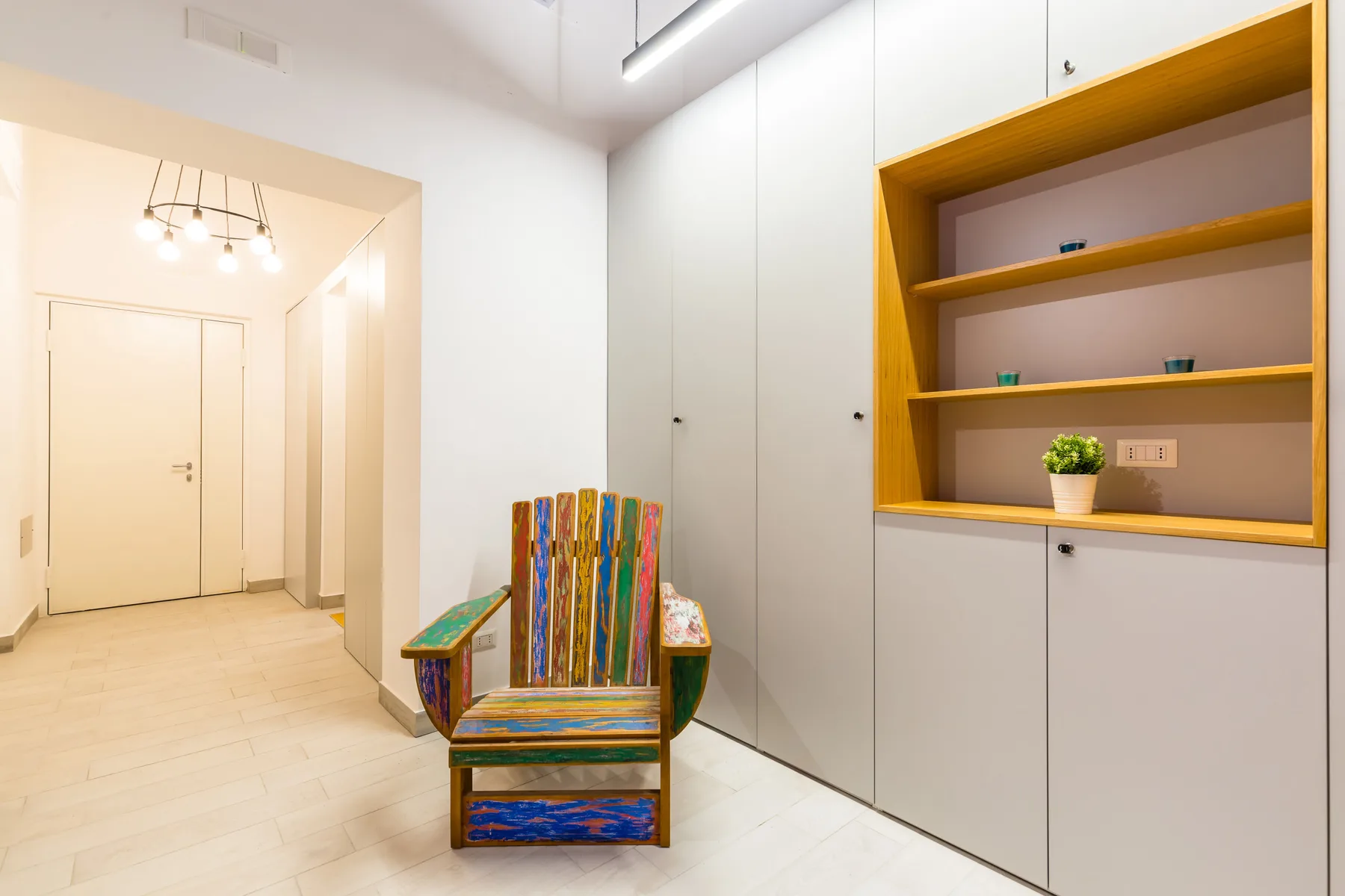 Una entrada luminosa con una silla colorida y estanterías empotradas.