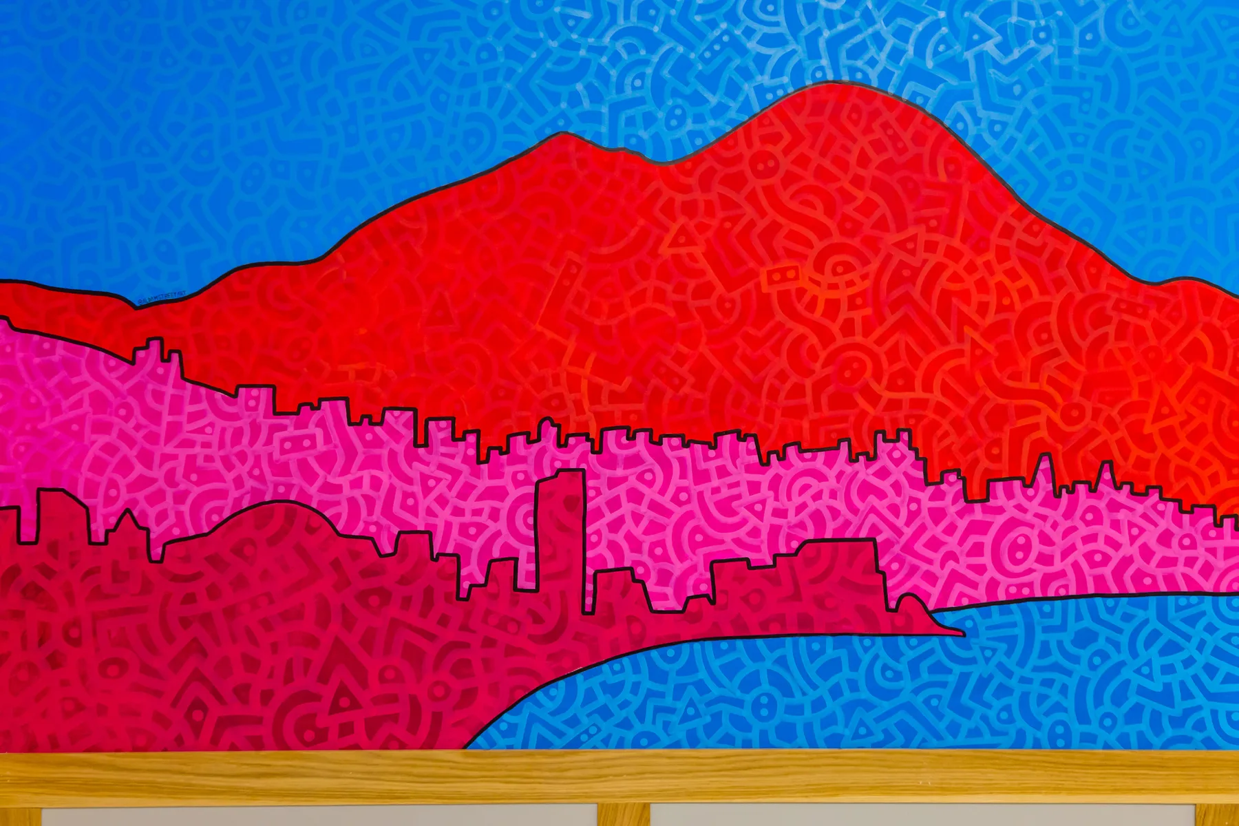 Un mural colorido muestra una montaña sobre el perfil de una ciudad y agua azul.