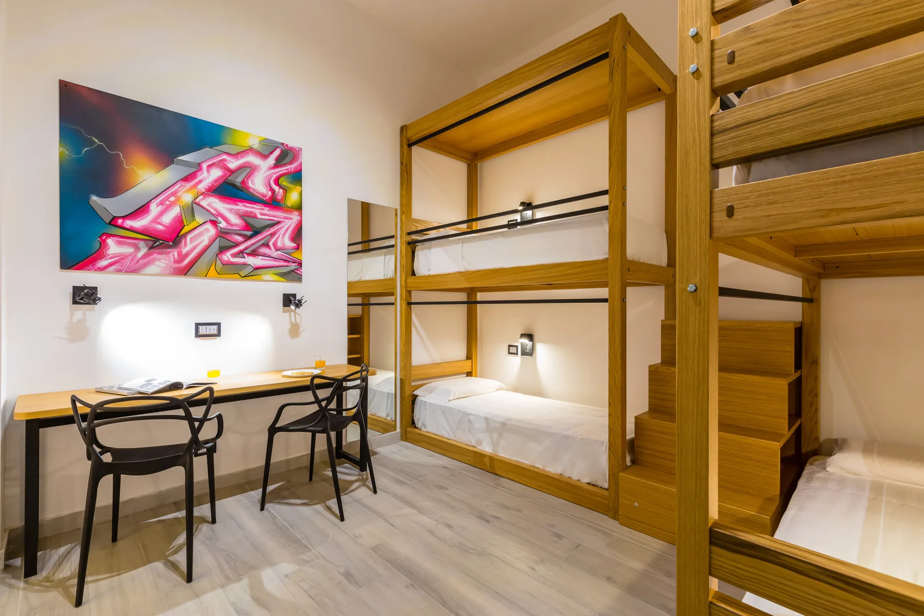 Un dormitorio con literas de madera, un escritorio y arte colorido en la pared.