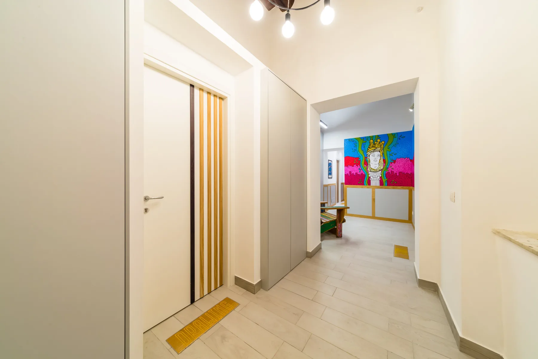 Un pasillo luminoso conduce a una habitación con arte colorido en la pared.