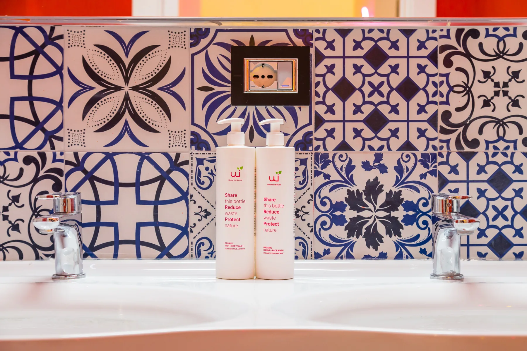 Un lavabo de baño con azulejos estampados azules y blancos y dos botellas.