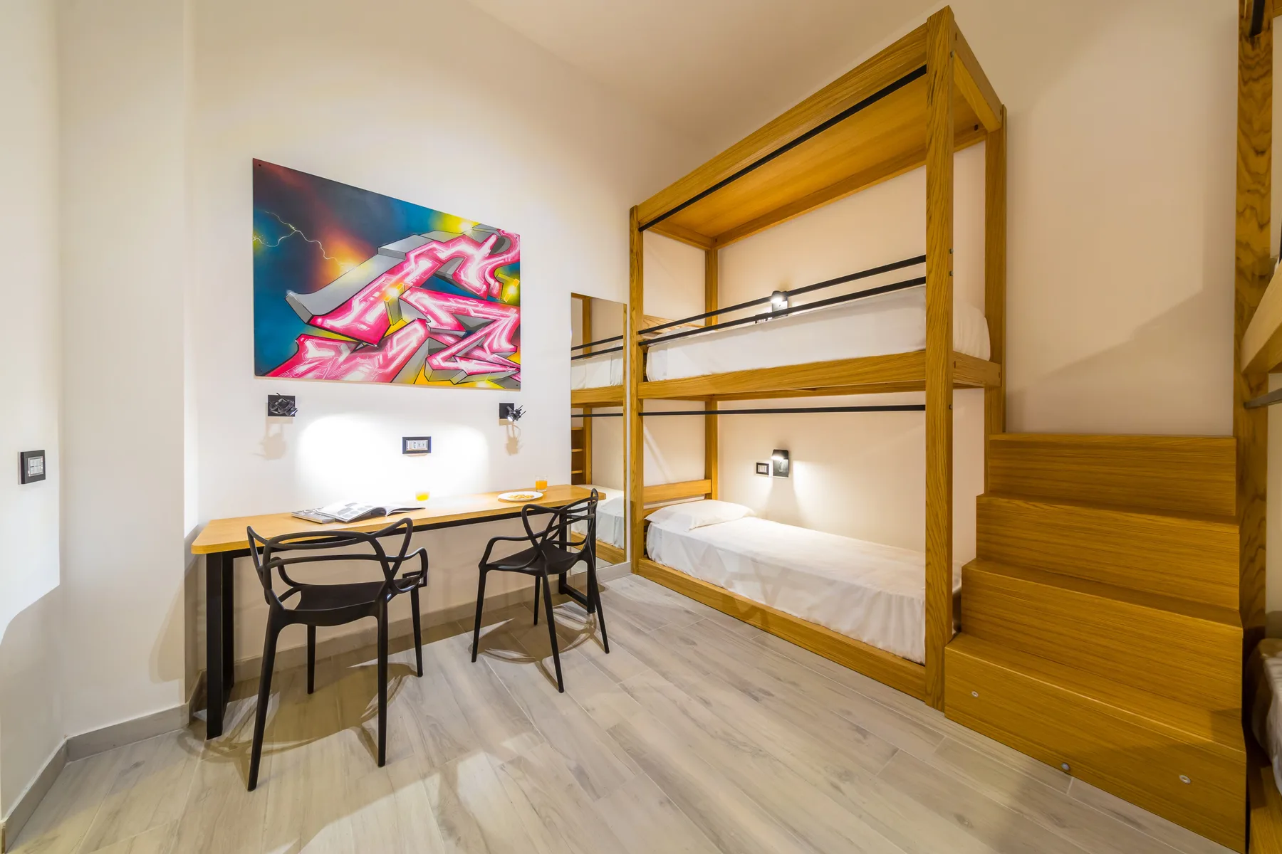 Una habitación con una litera de madera y un escritorio bajo una pintura colorida.