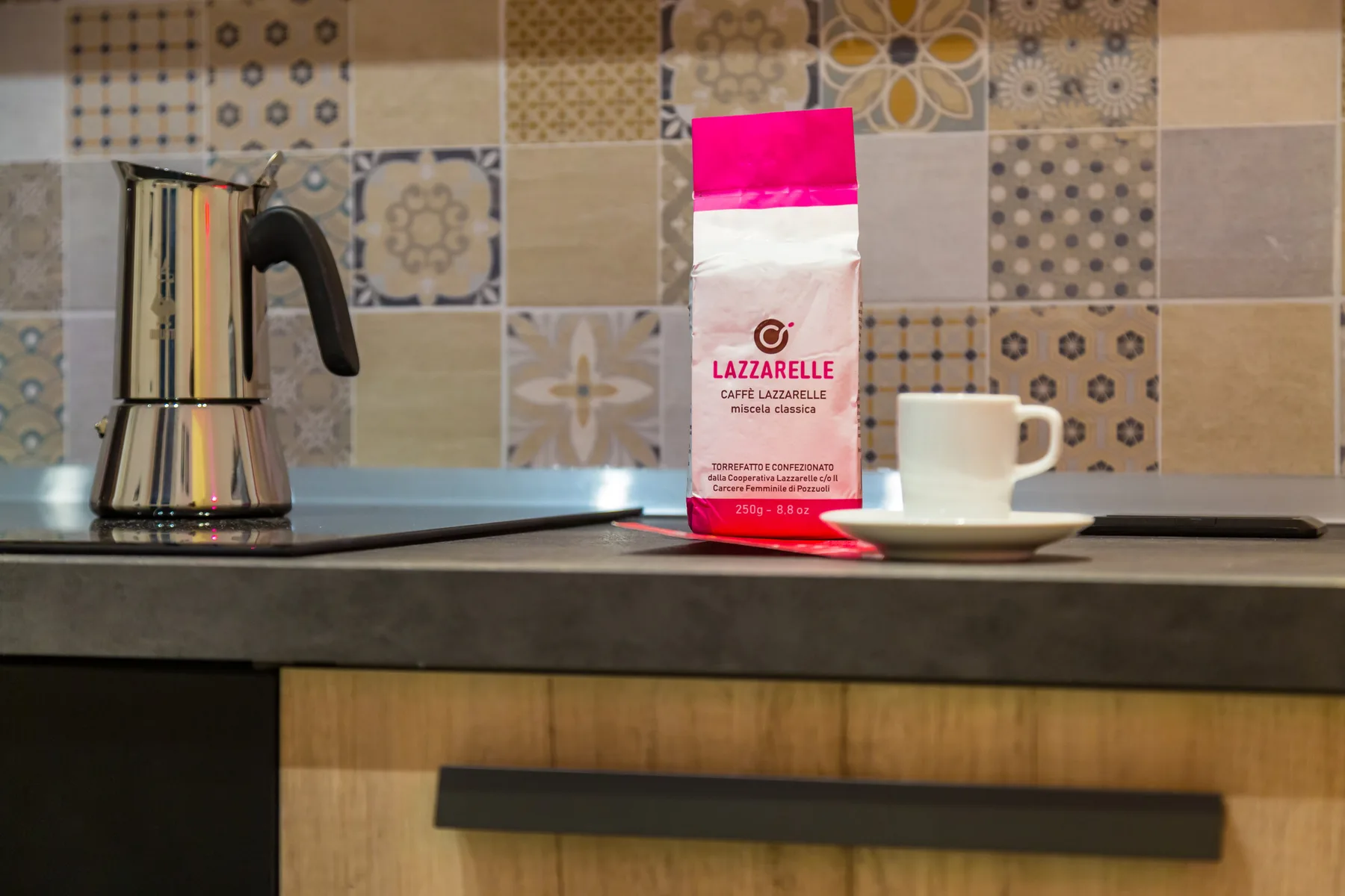 A kitchen counter with a coffee maker and cup against a patterned tile backsplash.