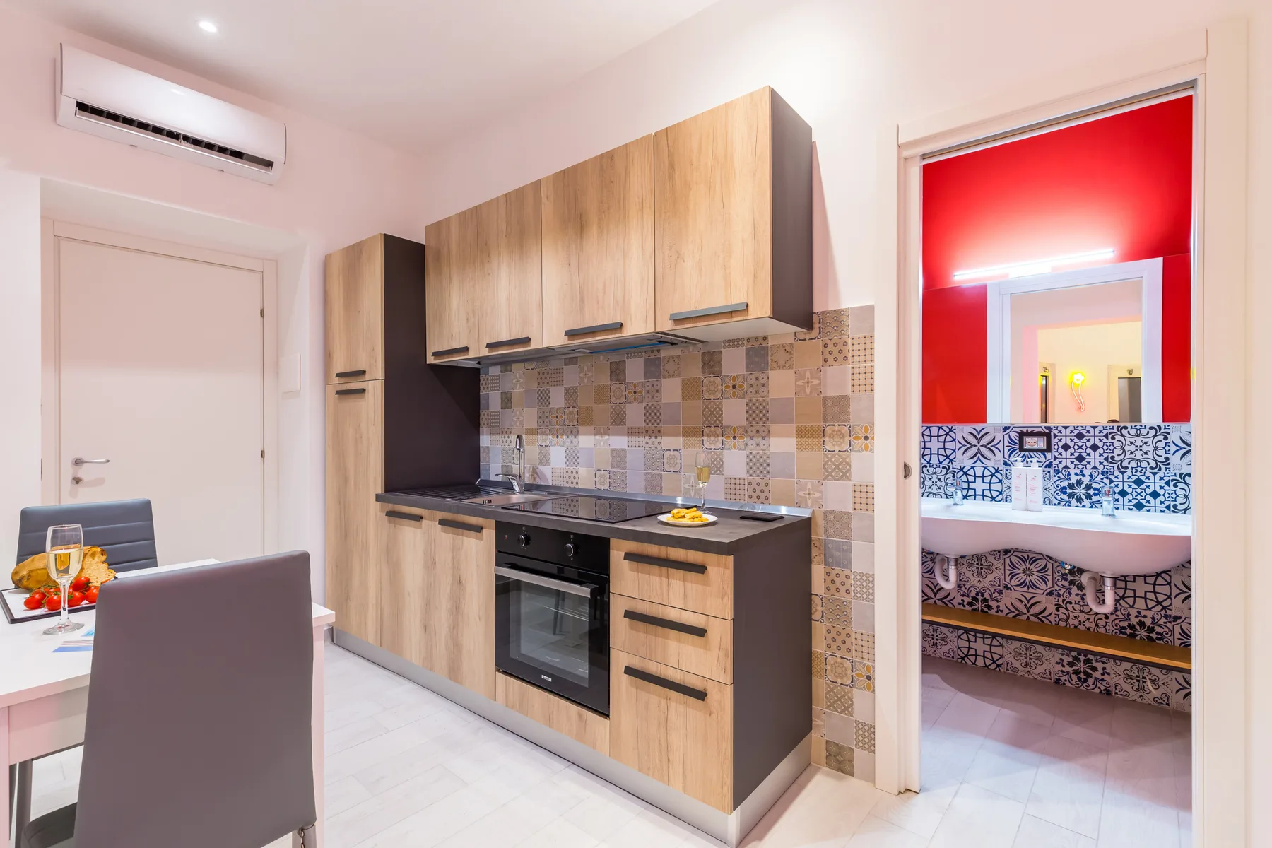 A compact kitchen with wood cabinets and a tiled backsplash opens onto a bathroom.