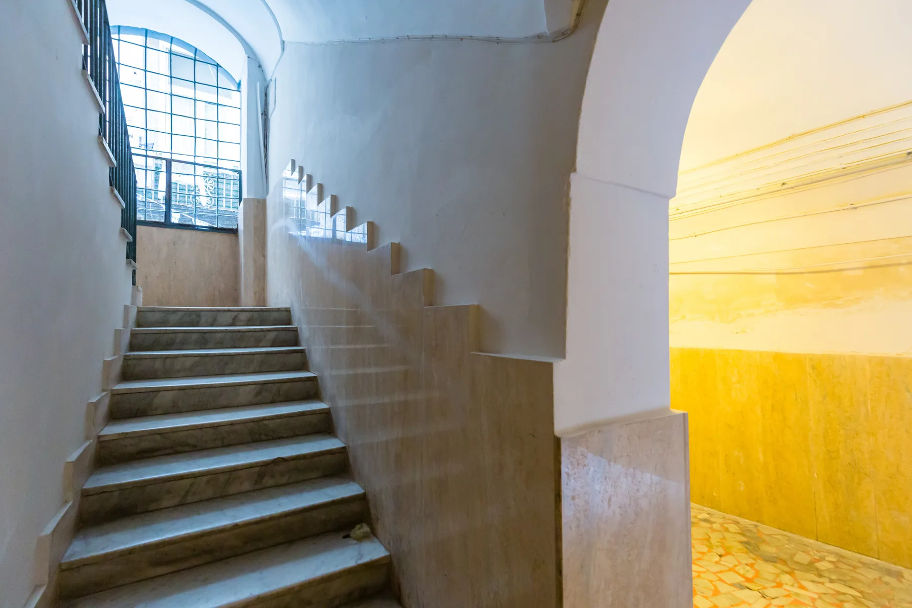 Una escalera sube junto a un arco que da a una habitación muy iluminada.