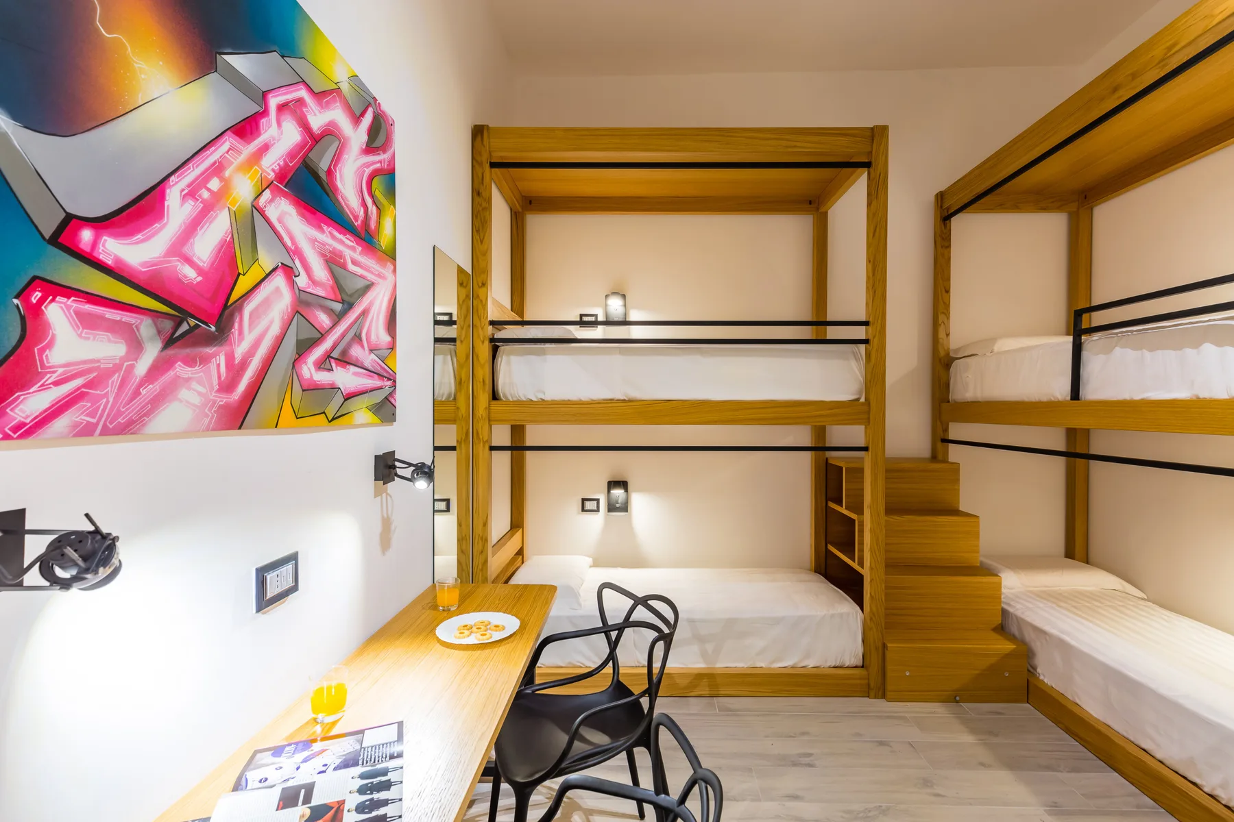 Una habitación con literas de madera, un escritorio y arte colorido en la pared.
