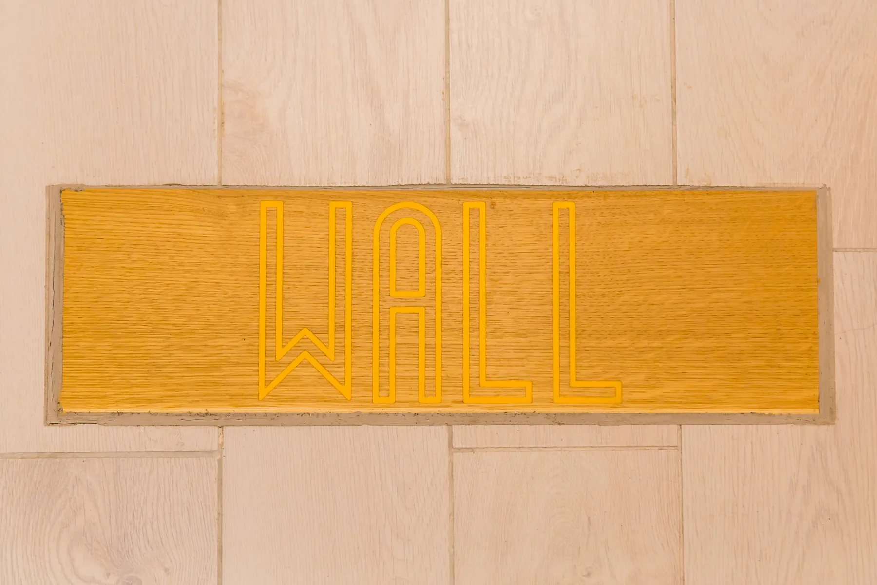 A wooden wall plaque displays the word “WALL” against pale paneling.