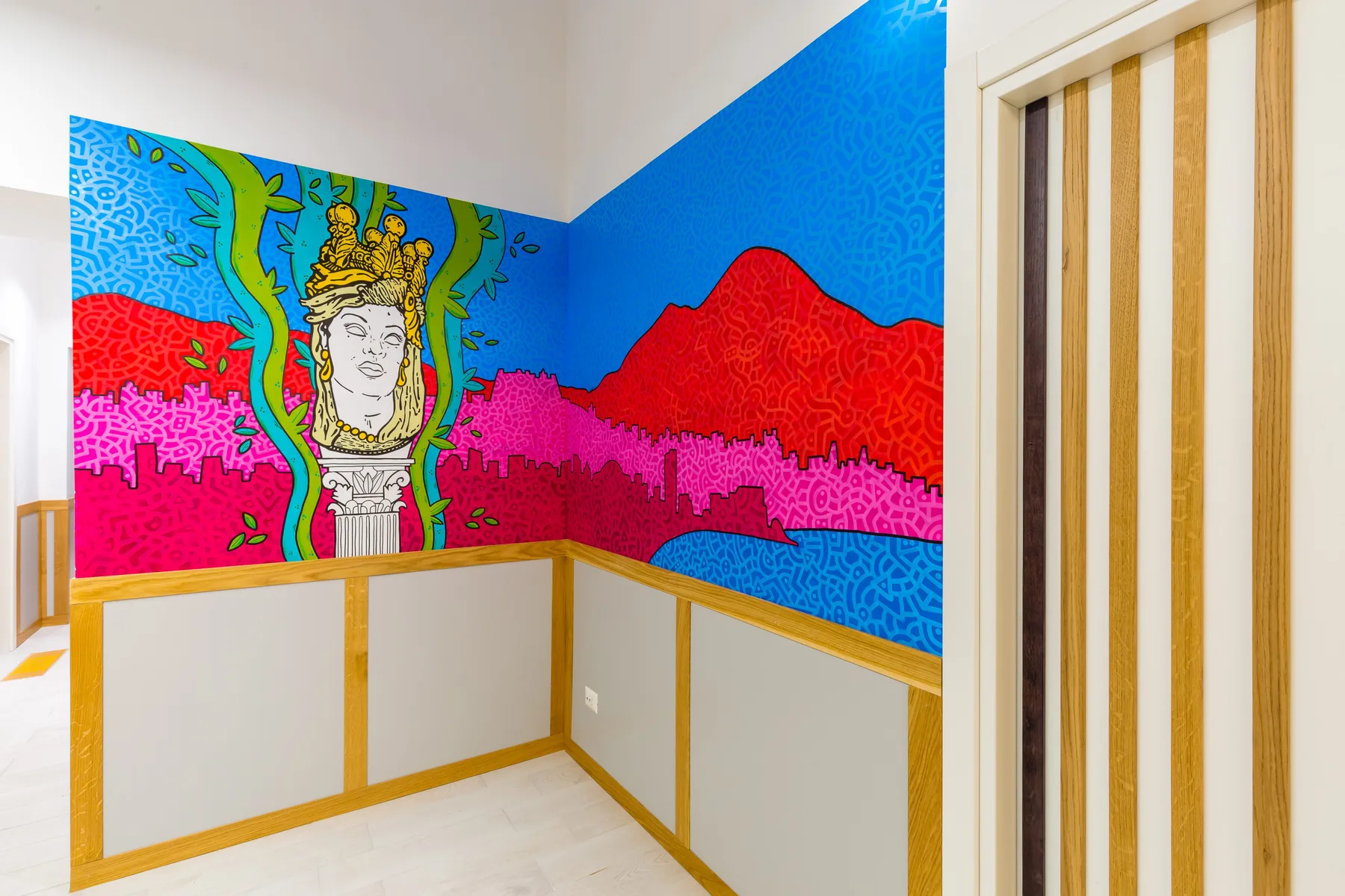 Un mural colorido decora las paredes de una esquina en una habitación luminosa.