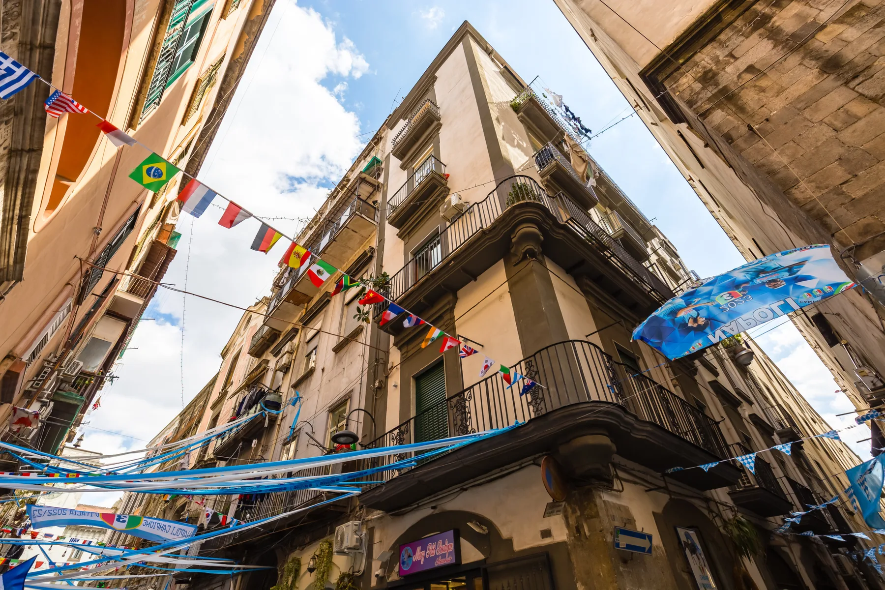 Una calle estrecha está bordeada de edificios altos y banderas de colores.