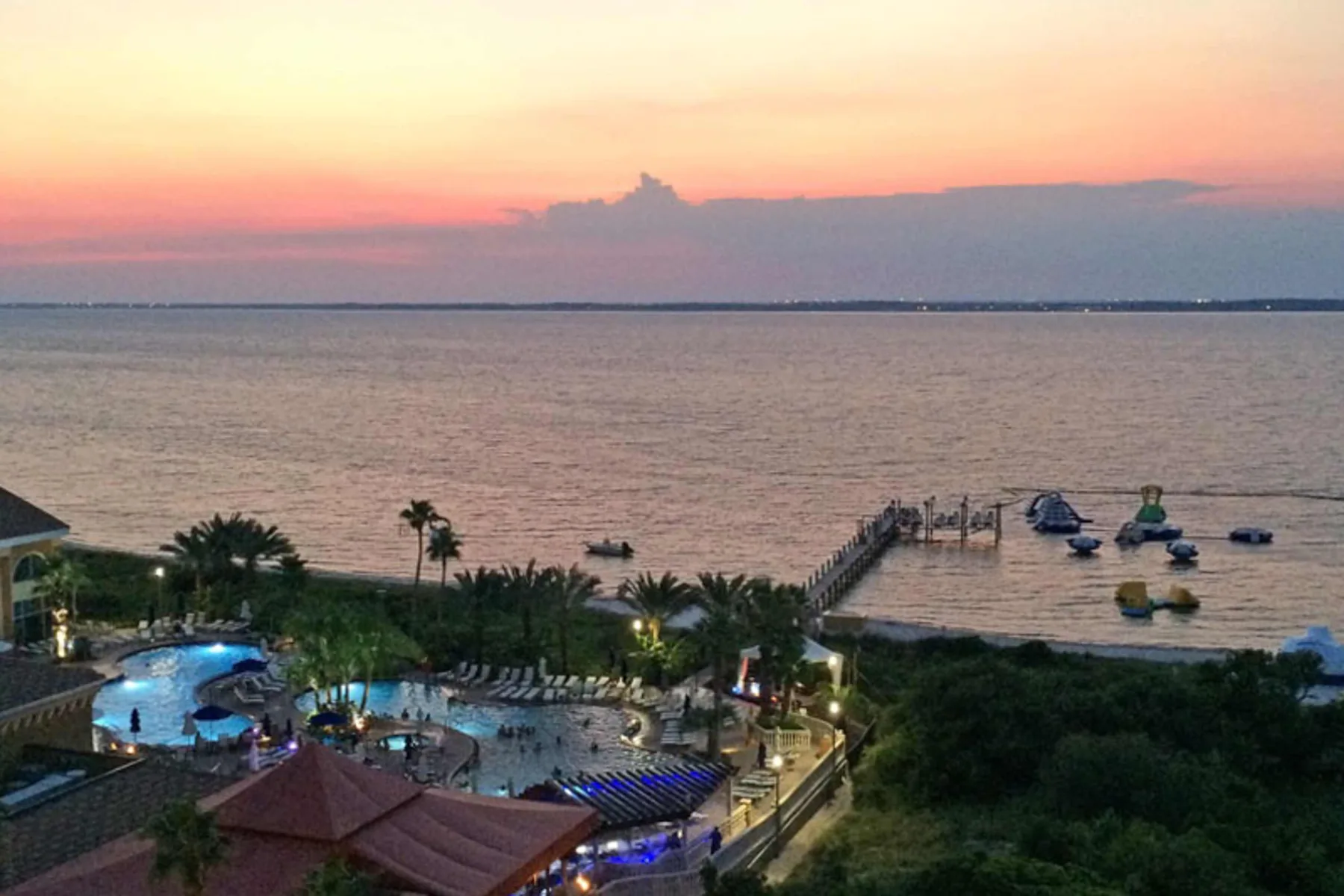Un complejo junto al agua al atardecer, con piscinas y barcos junto a la orilla.