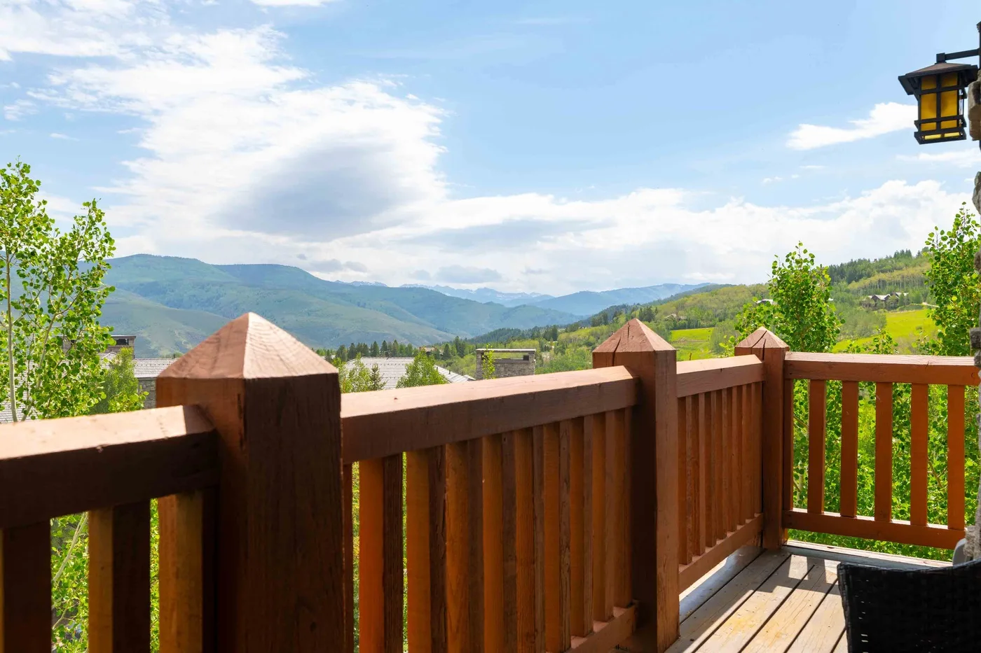 Una terraza de madera da a colinas verdes y montañas lejanas bajo un cielo parcialmente nublado.